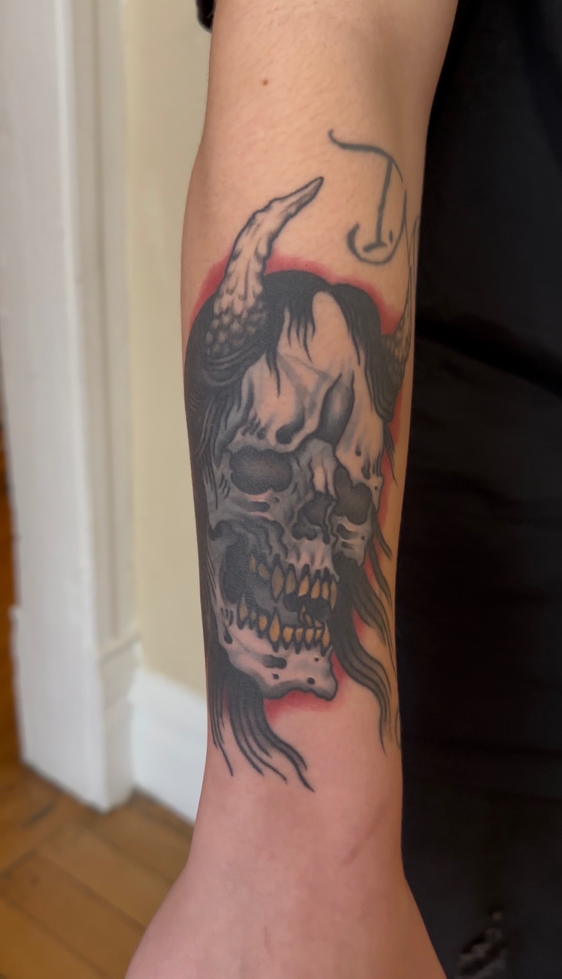 Neo-traditional tattoo of a horned skull with flowing hair and a red halo, on a forearm