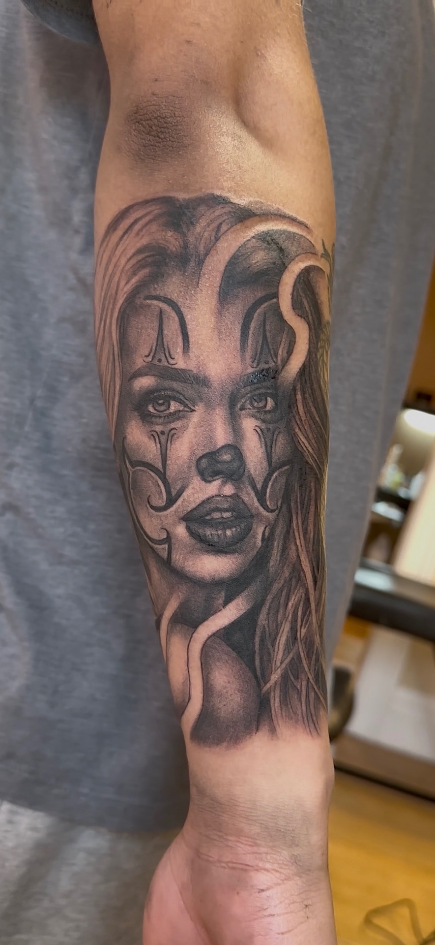 Black and grey Chicano-style portrait of a woman with clown markings, on an inner forearm