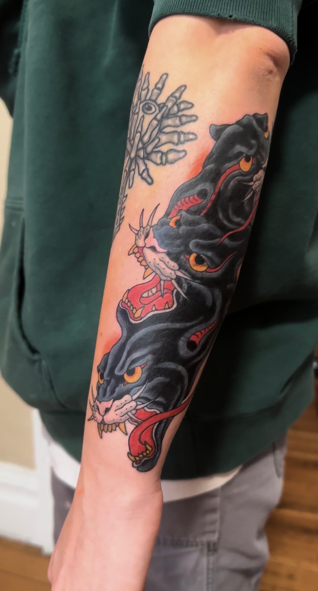 Neo-traditional tattoo of stacked panther heads with a skeletal hand, on a forearm